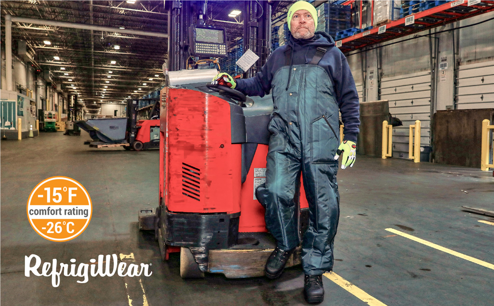 Man standing in a cold storage facility wearing the Econo-Tuff High Bib overalls in front of a forklift